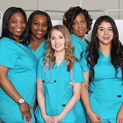 Two nurses wearing teal scrubs in front of a privacy curtain